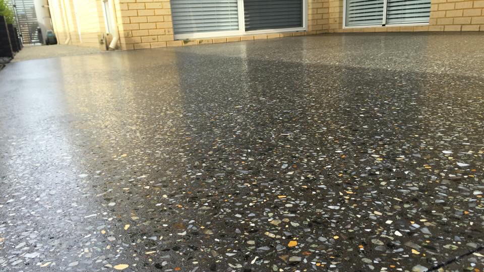 Close view across a glossy exposed aggregate slab beside a brick house