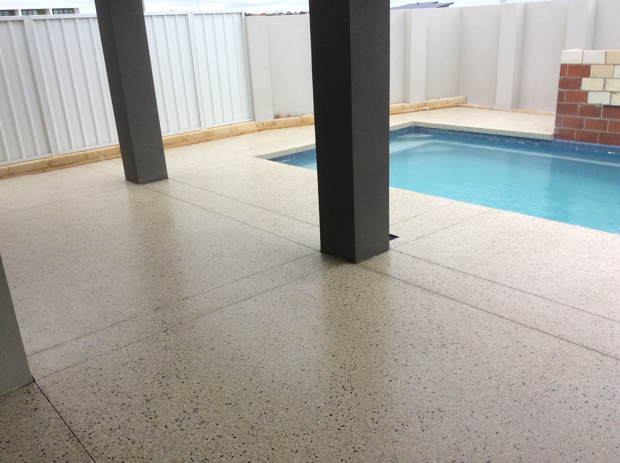 Exposed aggregate pool surround seen from under a covered alfresco